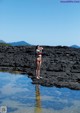 A woman in a bikini standing on a rock in the water.